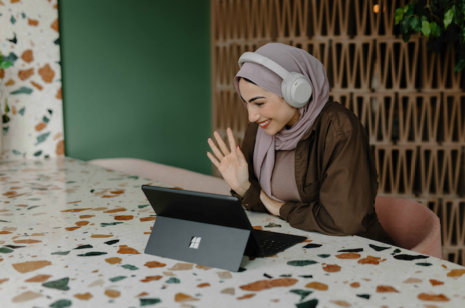 a woman with a head covering and headphones saying hi to someone on her tablet